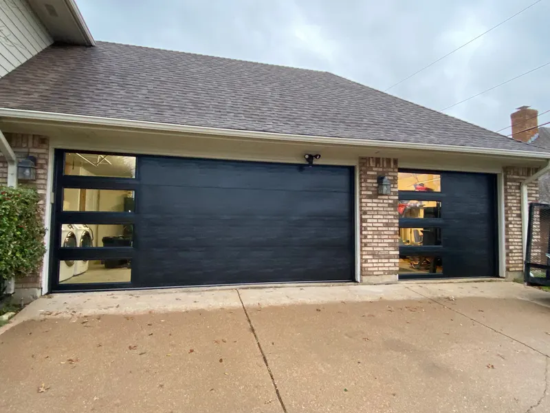 Two modern black flush-panel garage doors with window inserts on a DFW brick home