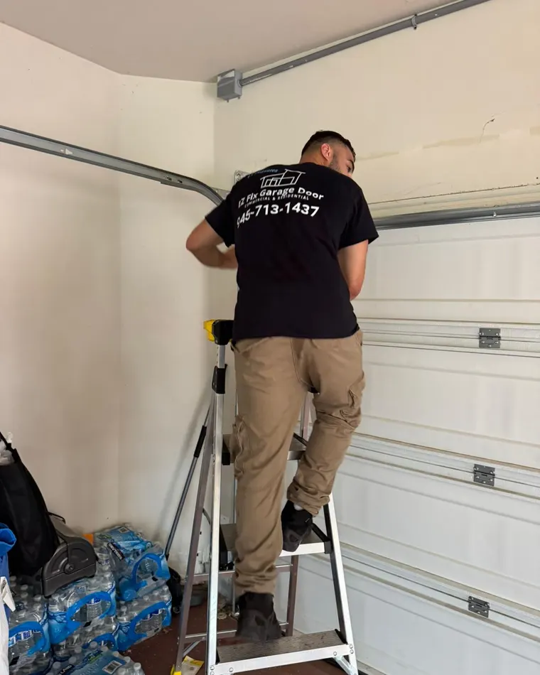 An EZ Fix technician in a branded EZ Fix Garage Door shirt working on a garage door track from a step ladder